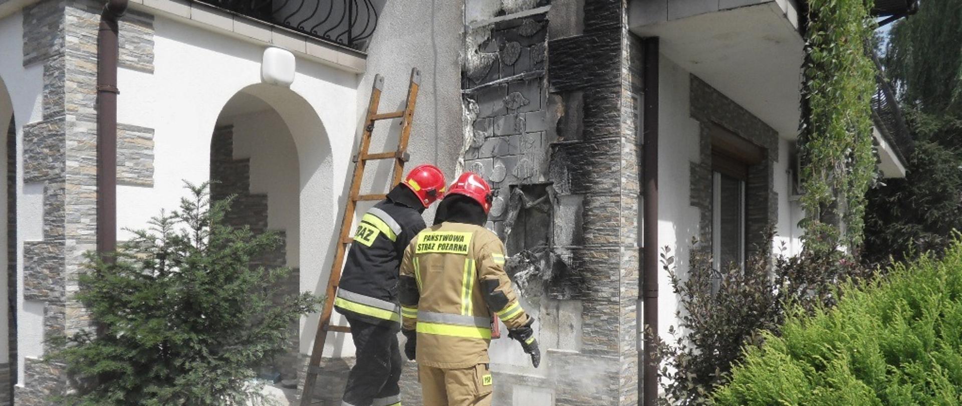 Na zdjęciu dwóch strażaków dokonujących rozbiórki nadpalonej izolacji termicznej budynku mieszkalnego