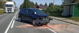 Na zdjęciu widać przód pojazdu opel, wycieki płynów eksploatacyjnych po kolizji, na drugim planie korek na DK73- droga zablokowana.