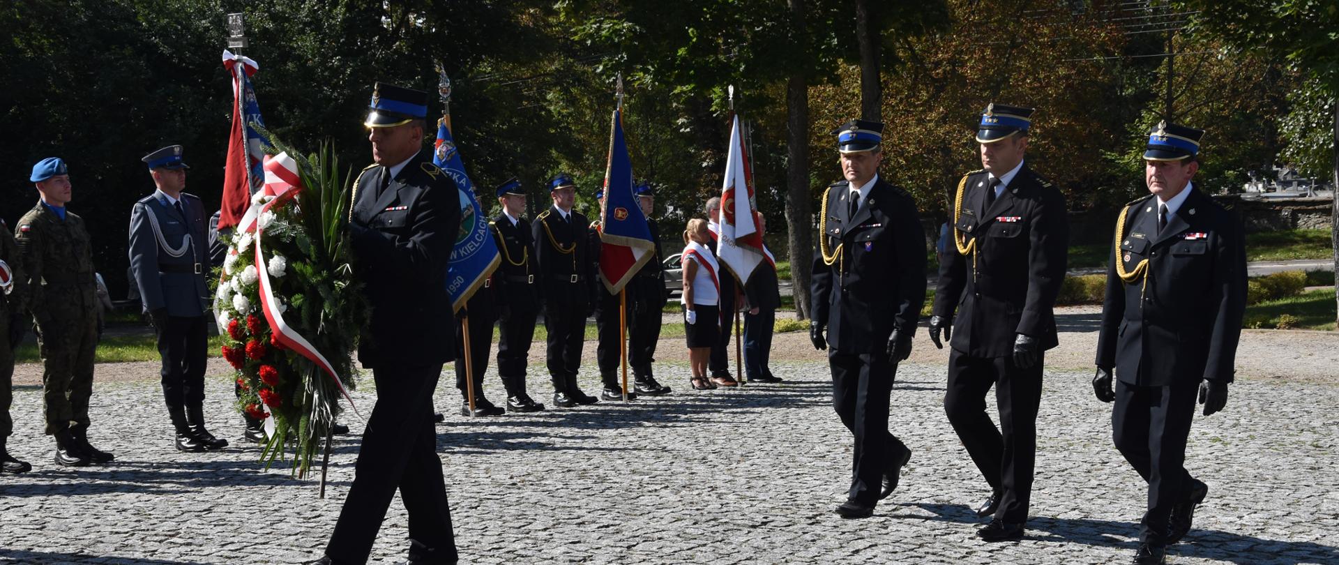 Zdjęcie przedstawia Komendanta Wojewódzkiego PSP w Kielcach oraz Komendanta Miejskiego PSP w Kielcach wraz z zastępcą w trakcie składania wieńca pod pomnikiem upamiętniającym wydarzenie z 11 września 2001r. 