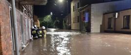 Zdjęcie przedstawia strażaków stojących w wodzie podczas działań związanych
z usuwaniem skutków ulewnych deszczy.
