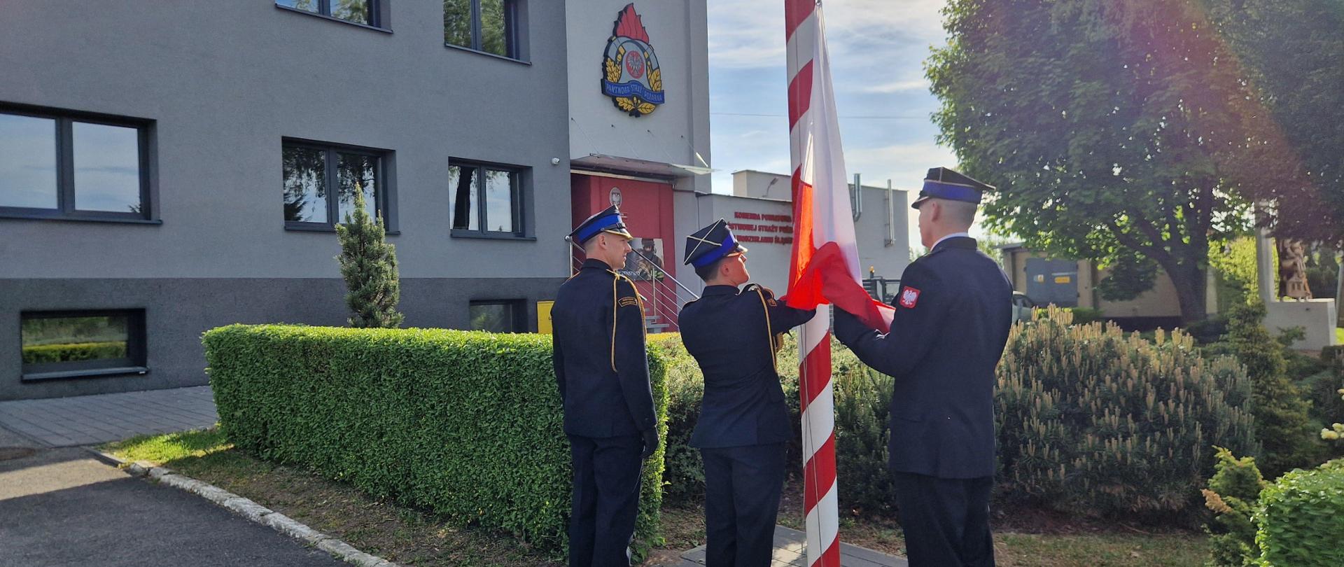Poczet flagowy w liczbie 3 strażaków dokonuje podniesienia flagi państwowej na maszcie przed budynkiem komendy