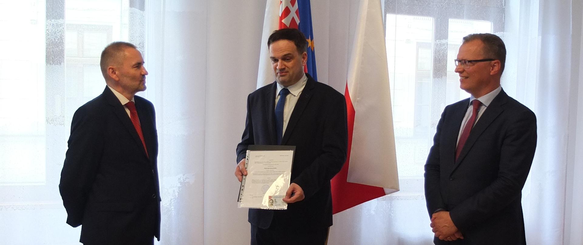 Zdjęcie przedstawia z lewej strony konsula RP Stanisław Kargul, Pavla Liškę z potwierdzeniem uzyskania Karty Polaka w rękach i ambasadora RP Krzysztofa Strzałkę na tle flag (od lewa) słowackiej, unijnej i polskiej 