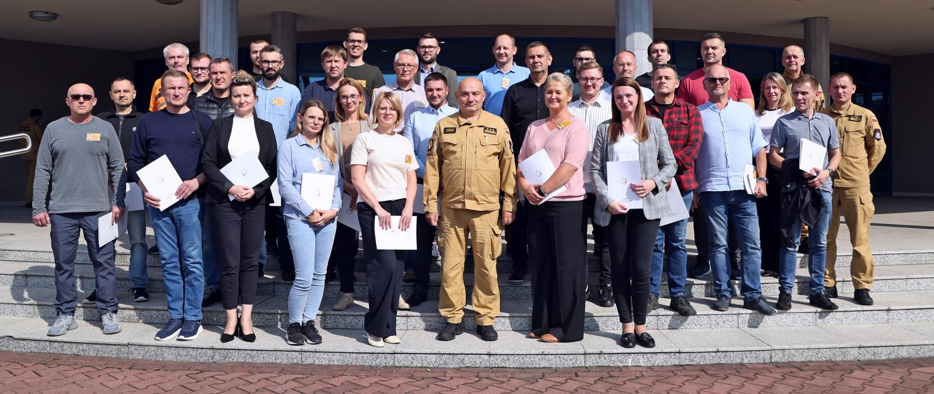 Pamiątkowe zdjęcie grupowe uczestników szkolenia dla inspektorów ochrony przeciwpożarowej (29 osób) w towarzystwie Komendanta Centralnej Szkoły PSP, kobiety oraz dwóch funkcjonariuszy CS PSP