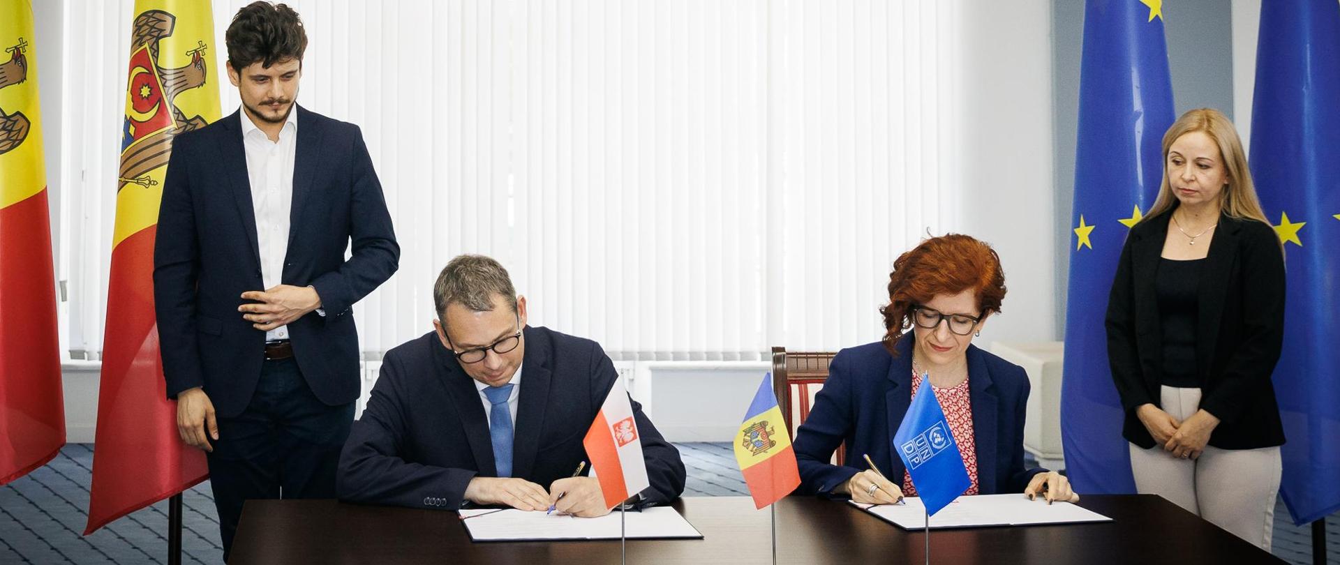 Two individuals signing documents in front of Moldova and EU flags.