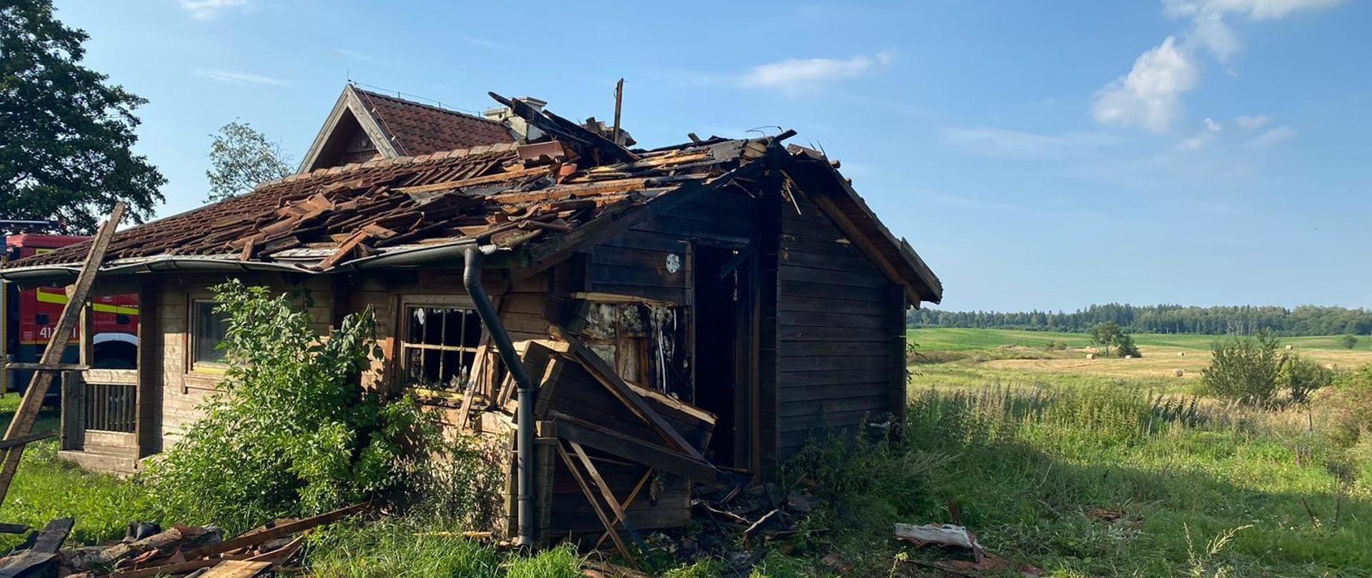 Drewniany domek pokryty dachówką na zielonej polanie. Słonecznie, niebieskie niebo.