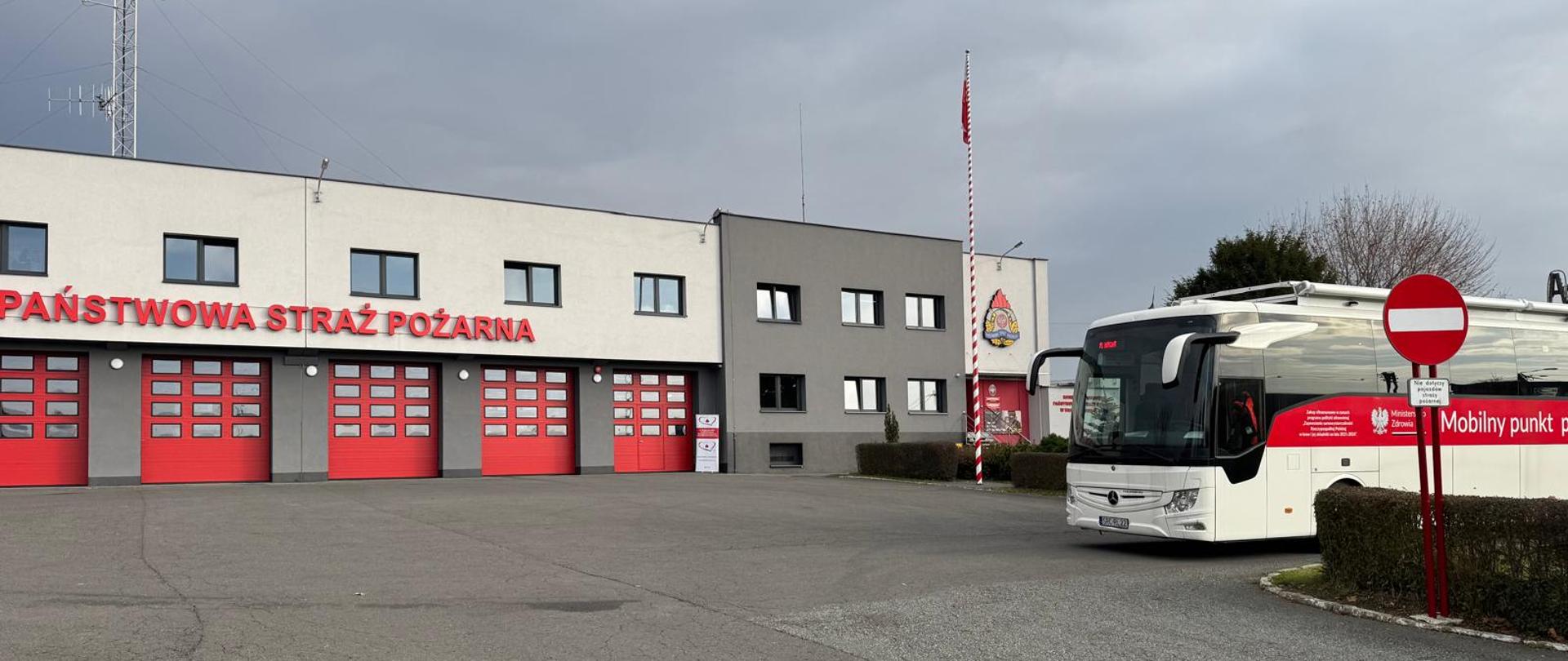 Autobus z centrum krwiodawstwa na tle budynku komendy straży pożarnej