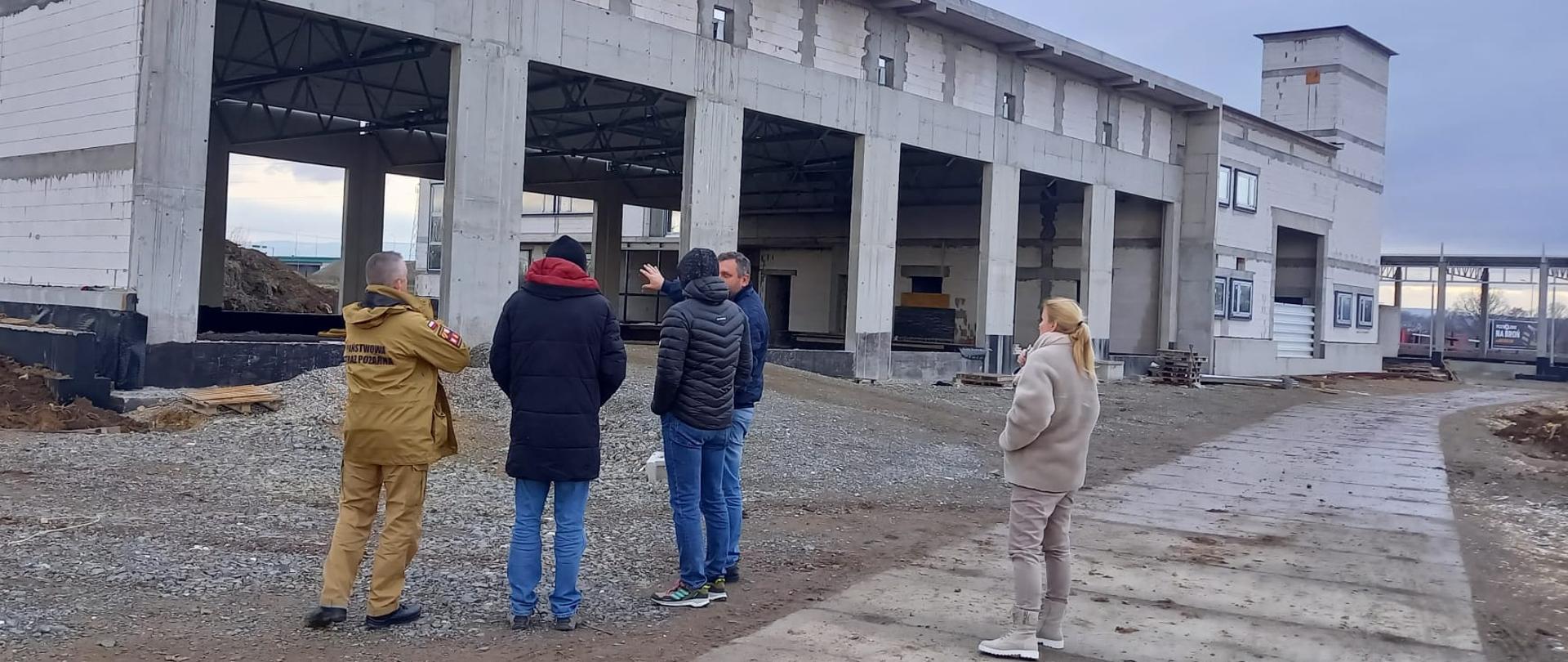 Widok na plac budowy. Przed budynkiem w stanie surowym stoi czterech mężczyzn oraz jedna kobieta.