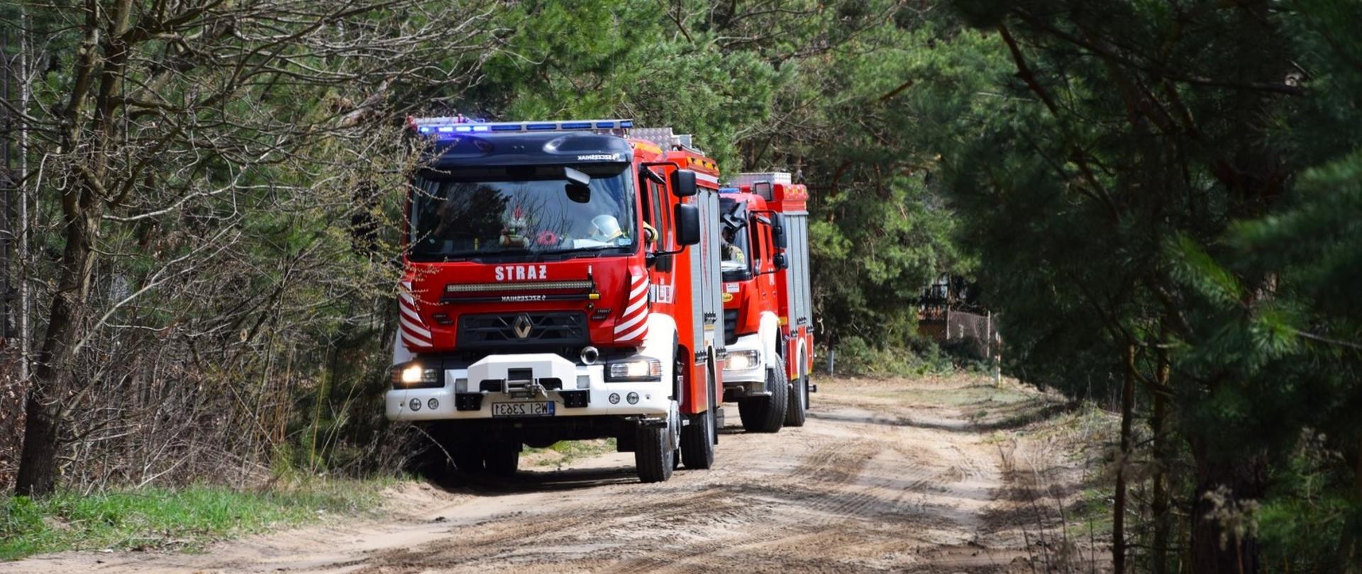 Na zdjęciu widoczne 2 pojazdy pożarnicze w lesie na drodze piaskowej