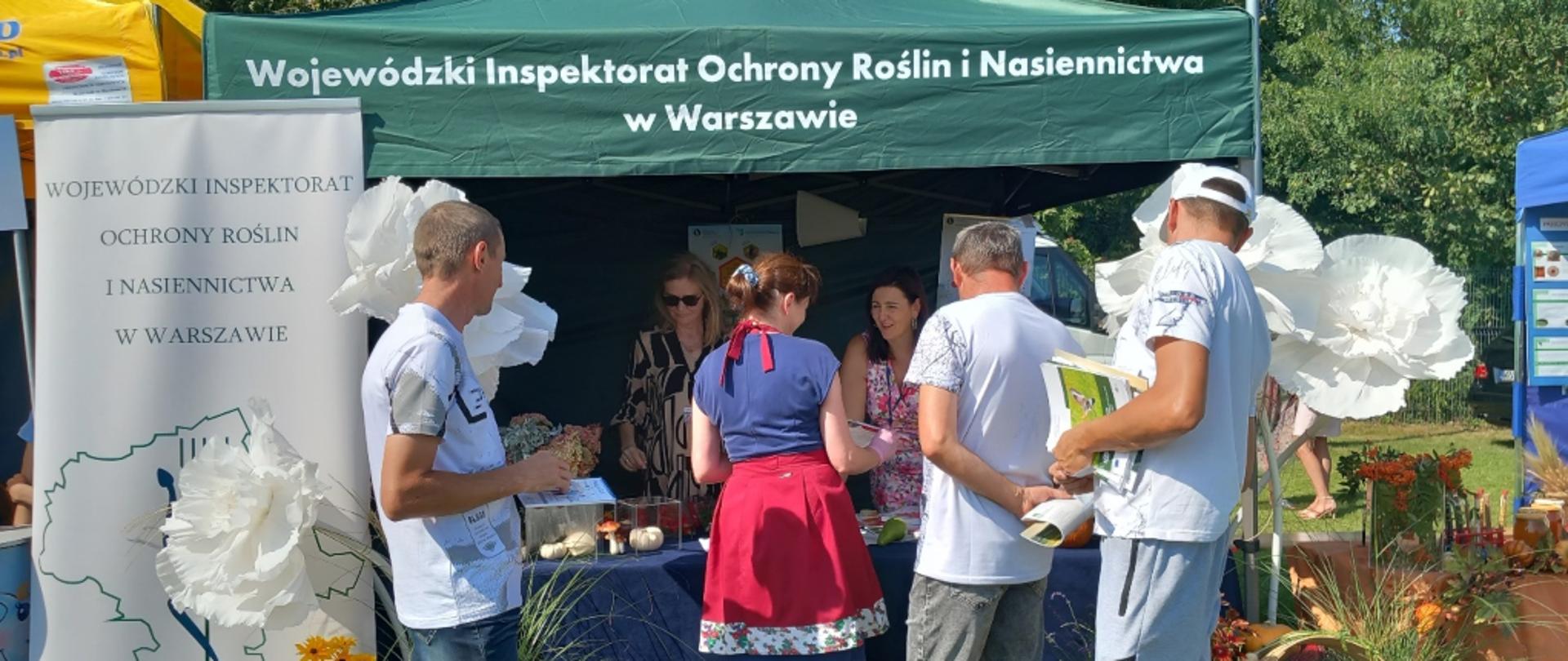 Uczestnicy dożynek przy przystrojonym roślinami ozdobnymi oraz koszami płodów rolnych stoisku promocyjno-informacyjnym Wojewódzkiego Inspektoratu Ochrony Roślin i Nasiennictwa w Warszawie, Oddziału w Radomiu