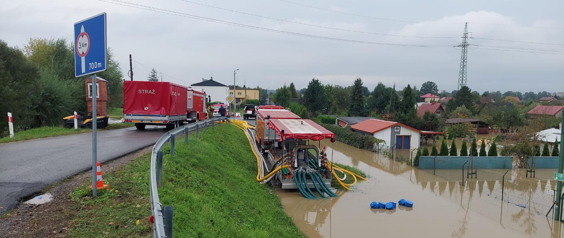 Zdjęcie przedstawia działania strażaków podczas pompowania wody z rozlewiska za pomocą pompy wysokiej wydajności