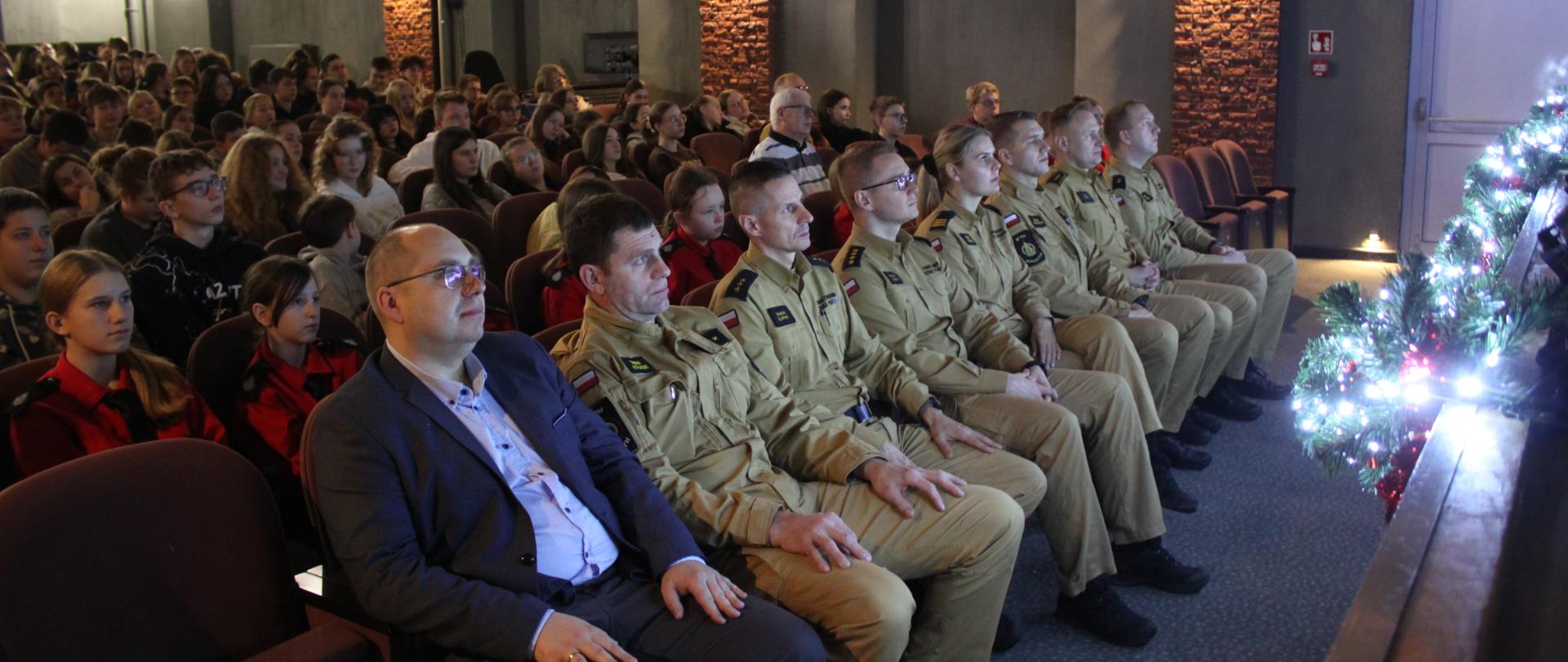 Zdjęcie przedstawia widzów podczas seansu w kinie. W tle wyświetlany jest dokument. na pierwszym planie widzowie siedzący na fotelach.