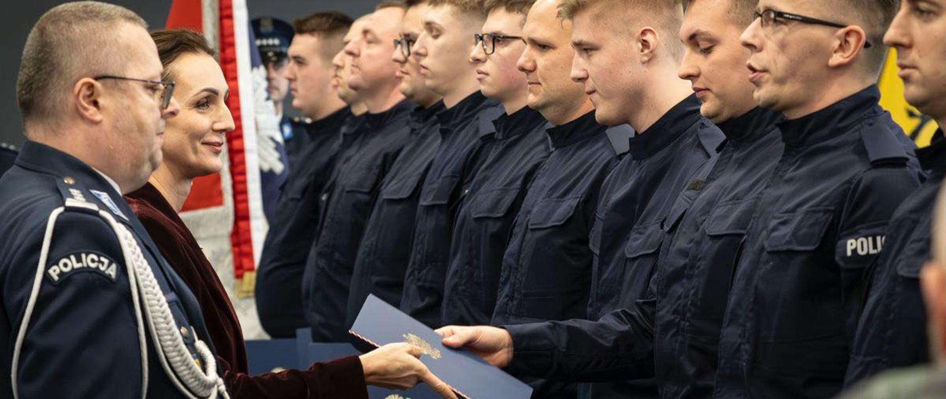 w szeregu stoi kilkunastu policjantów . wojewoda wręcza im teczki z gratulacjami z okazji ślubowania