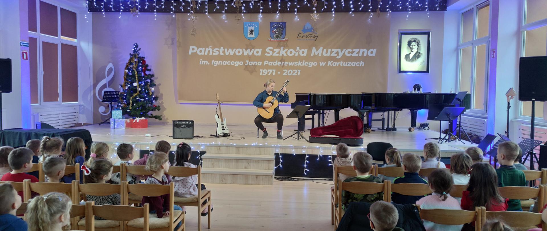 nauczyciel na scenie gra na gitarze przedszkolakom