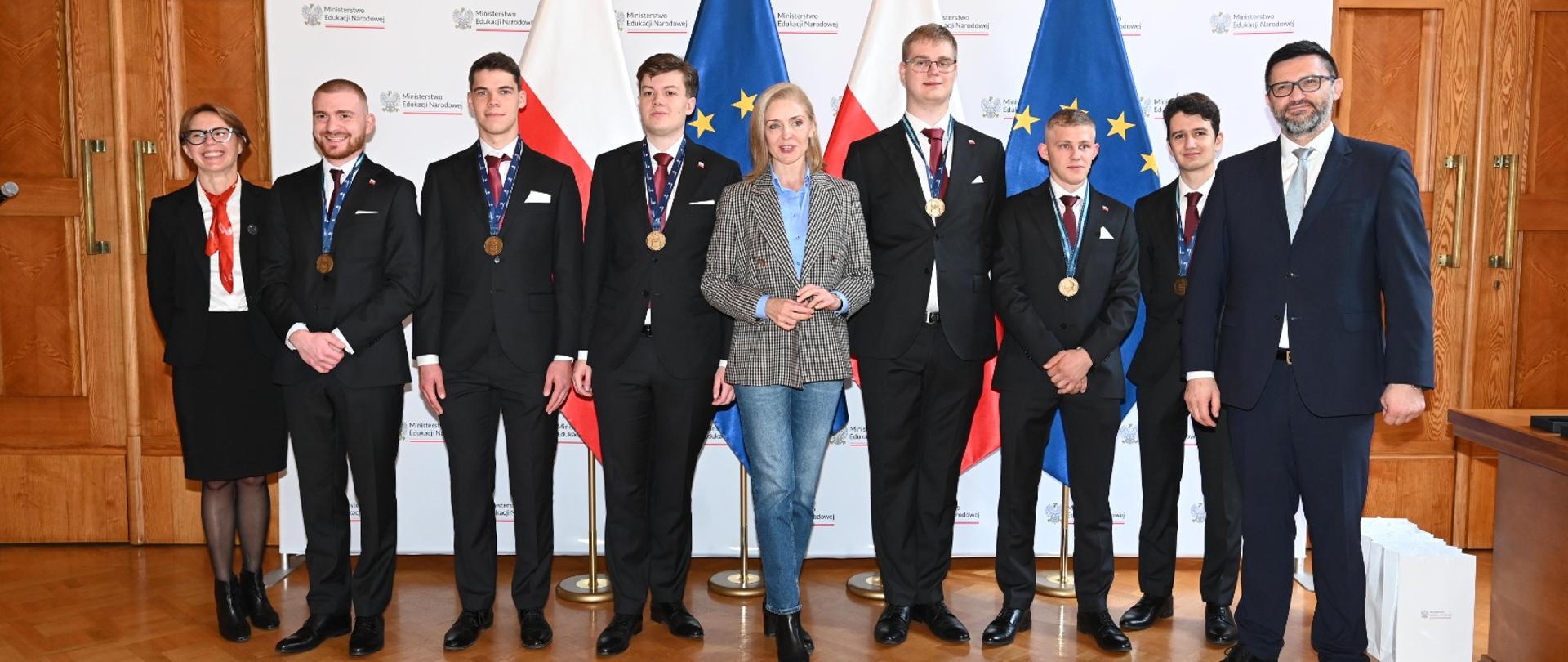 Zdjęcie zbiorowe, na tle białej ścianki z napisem Ministerstwo Edukacji Narodowej stoi wiceminister Mucha z Laureatami WorldSkills 2024 Lyon