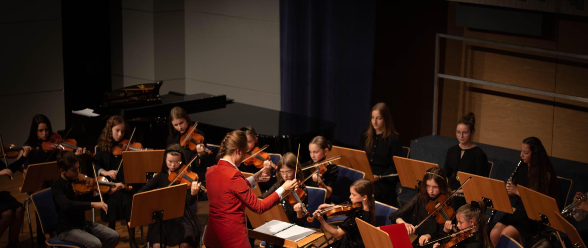 Zdjęcie występu Orkiestry PSM I st. z dyrygentką prowadzącą koncert - zdjęcie wykonane z prawej strony balkonu