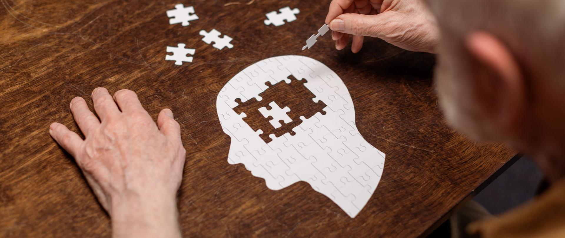 Na zdjęciu jest starszy mężczyzna układający puzzle w kształcie głowy człowieka.