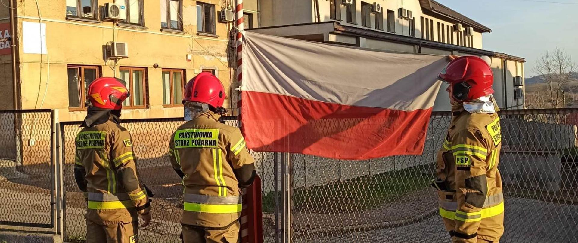 Obchody Narodowego Święta Niepodległości w KP PSP w Brzozowie. Strażacy uroczyście wciągają flagę na maszt.