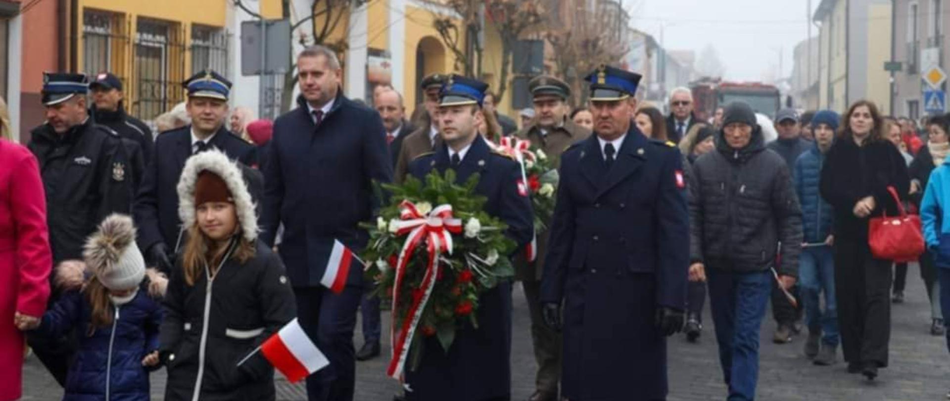 Zdjęcie przedstawia uroczysty przemarsz mieszkańców z wieńcami w Chmielniku.