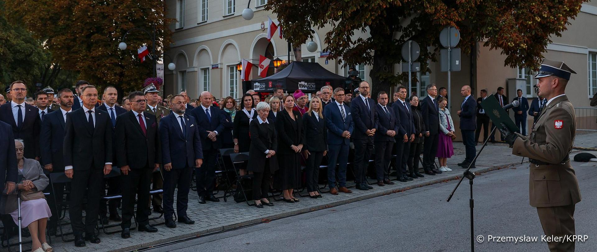 uczestnicy uroczystości w tym Prezydent RP, wojewoda łódzki, i inni stoją na placu, na przeciwko nich żołnierz , w tle budynek 