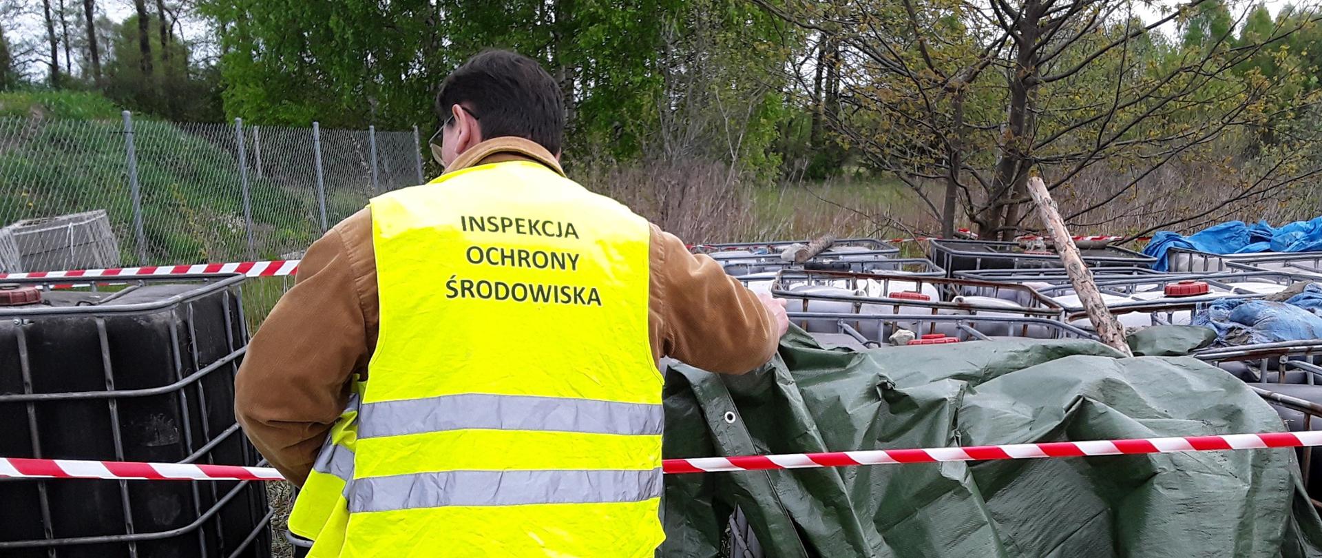 Inspektor Wojewódzkiego Inspektoratu Ochrony Środowiska w Warszawie prowadzi oględziny pojemników z odpadami o pojemności 1000 l porzuconych na otwartym terenie.