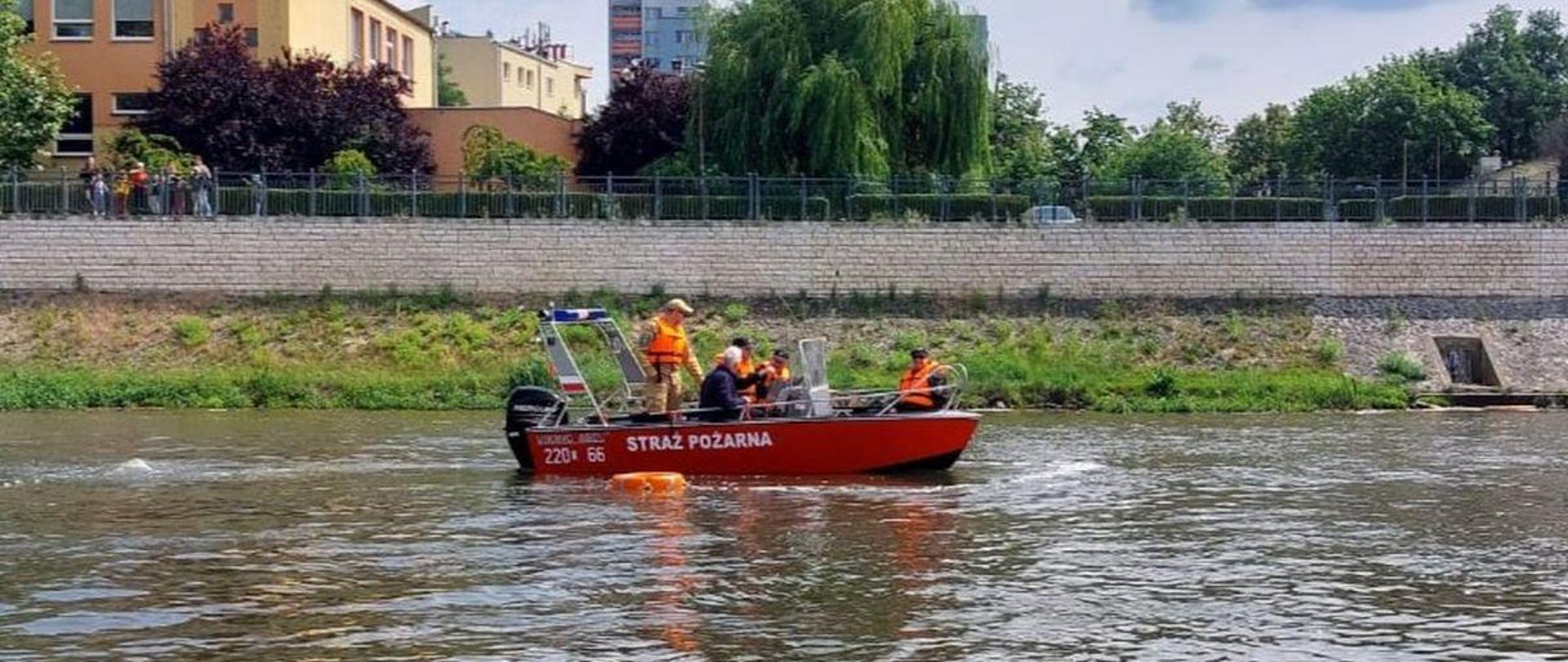 Strażacy Państwowej Straży Pożarnej oraz ochotniczych straży pożarnych ubrani w kamizelki ratownicze siedzą na łodzi podczas szkolenia na patent sternika motorowodnego. Łódź z napisem straż pożarna znajduje się na Odrze w Opolu.