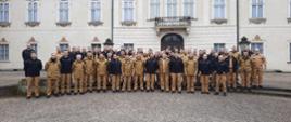 strażacy w mundurach w kolorze piaskowy, kilku w czarnych polarach pozują do zdjęcia na tle zabytkowego pałacu w Nieborowie