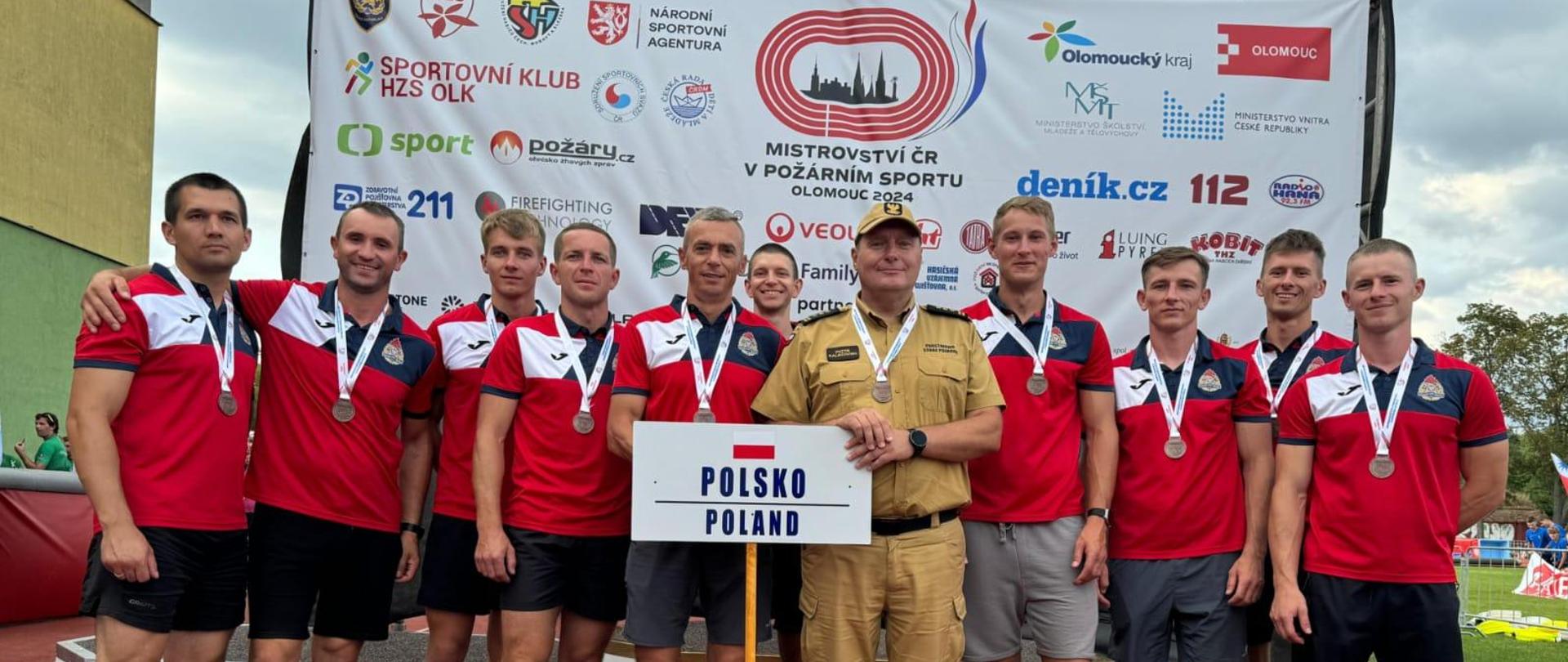 Reprezentacja Polski wraz z opiekunem pozuje do zdjęcia z tabliczką, na której znajduje się napis Polska Poland. Zawodnicy mają zawieszone na szyi medale.