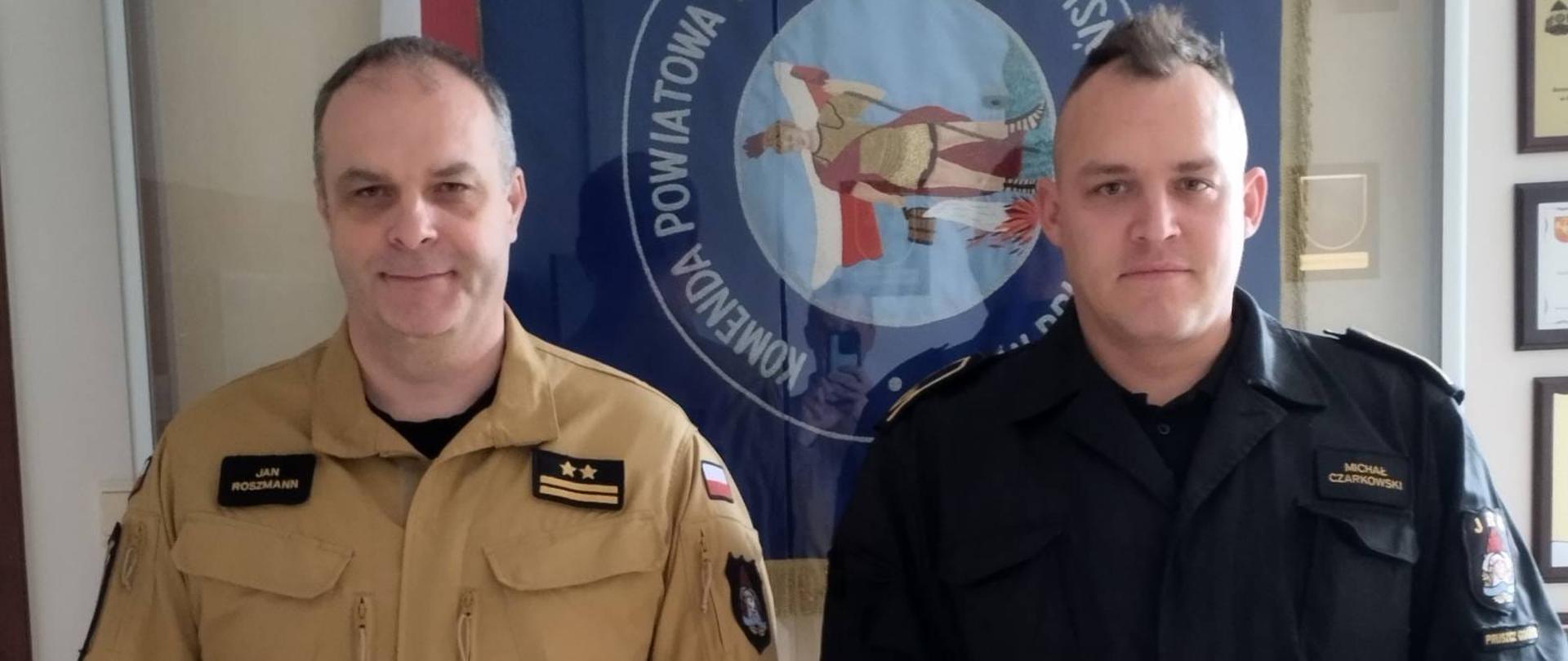Zdjęcie przedstawia nowo mianowanego zastępcę dowódcy JRG w Pruszczu Gdańskim oraz Komendanta powiatowego PSP w Pruszczu Gdańskim na tle sztandaru Komendy.