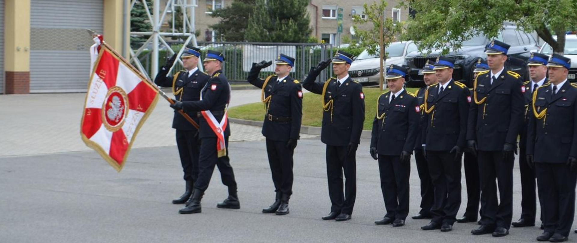 Na zdjęciu widoczny pododdział pożarniczy Komendy Powiatowej Państwowej Straży Pożarnej w Głubczycach w dwuszeregu podczas oddawania honory w związku z odgrywaniem Hymnu Państwowego.