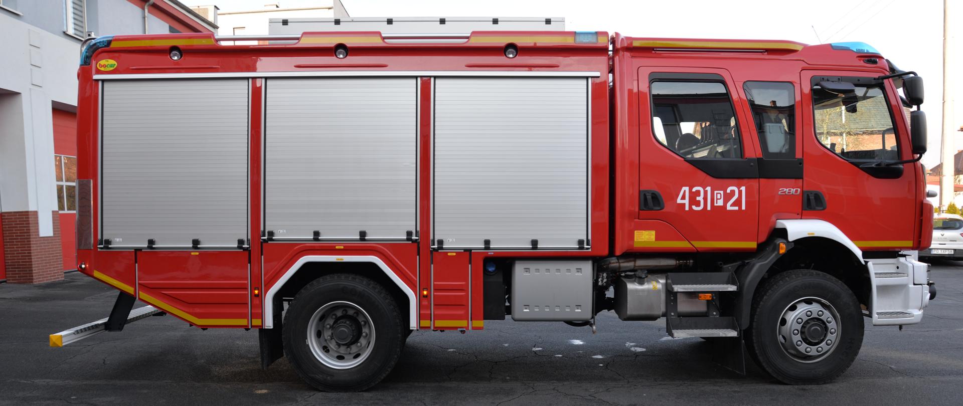 Zdjęcie przedstawia nowy samochód straży pożarnej. Samochód jest czerwony, stoi na placu wewnętrznym komendy straży pożarnej.