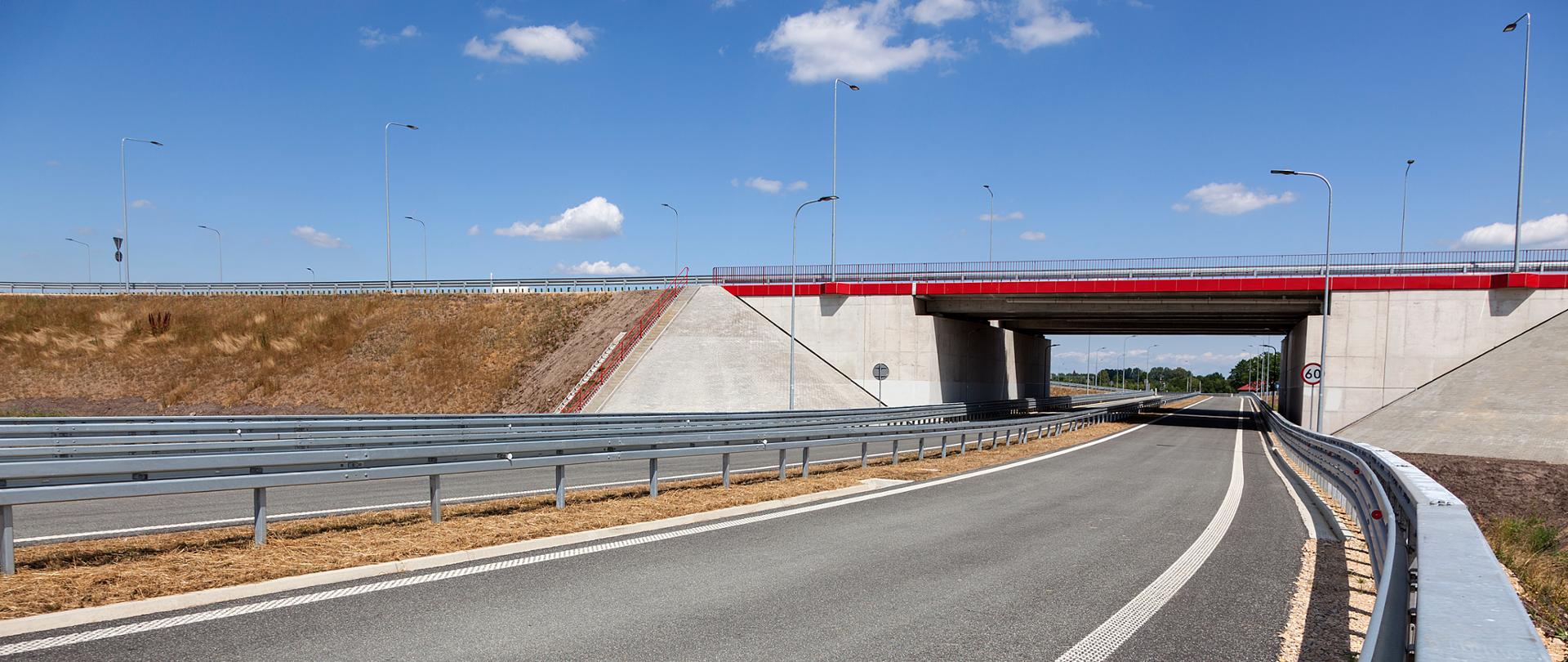 Fotografia wiaduktu drogowego pod autostradą A1. Belki gzymsowe obiektu i poręcze wykonano w kolorze czerwonym.