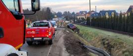 Zdjęcie zrobione dzień. Na zdjęciu widać samochody strażackie, policję, karetkę pogotowia , strażaków i rozbity samochód osobowy w rowie. 