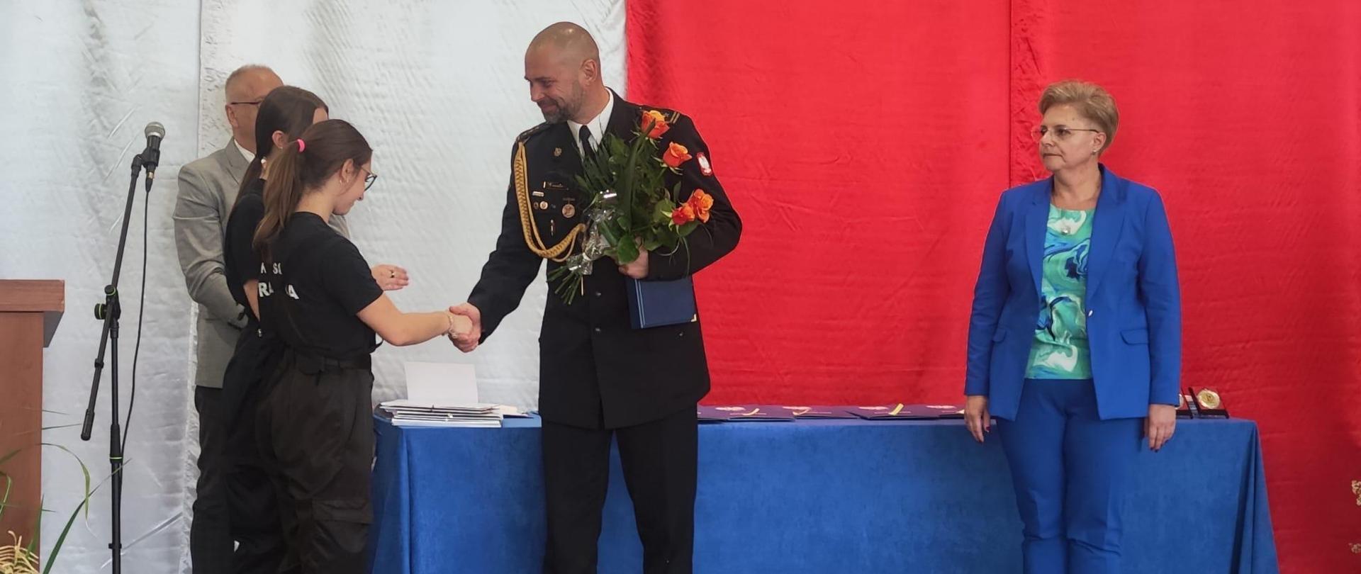 Wręczenie świadectw ukończenia roku szkolnego na sali gimnastycznej IV LO w Wałbrzychu. W tle biało czerwona flaga