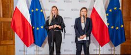 Na tle białej ścianki z napisem Ministerstwo Edukacji Narodowej oraz flag Polski i UE stoi przy mikrofonie minister Barbara Nowacka, a obok niej wiceminister Paulina Piechna-Więckiewicz