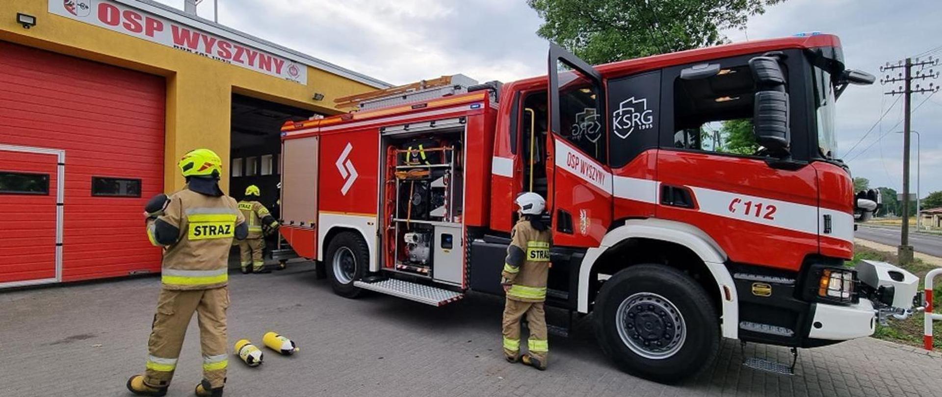 samochód gaśniczy osp stojący przed garażem obok ratownicy osp