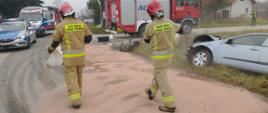 Strażacy posypują sorbentem rozlane paliwo na drodze