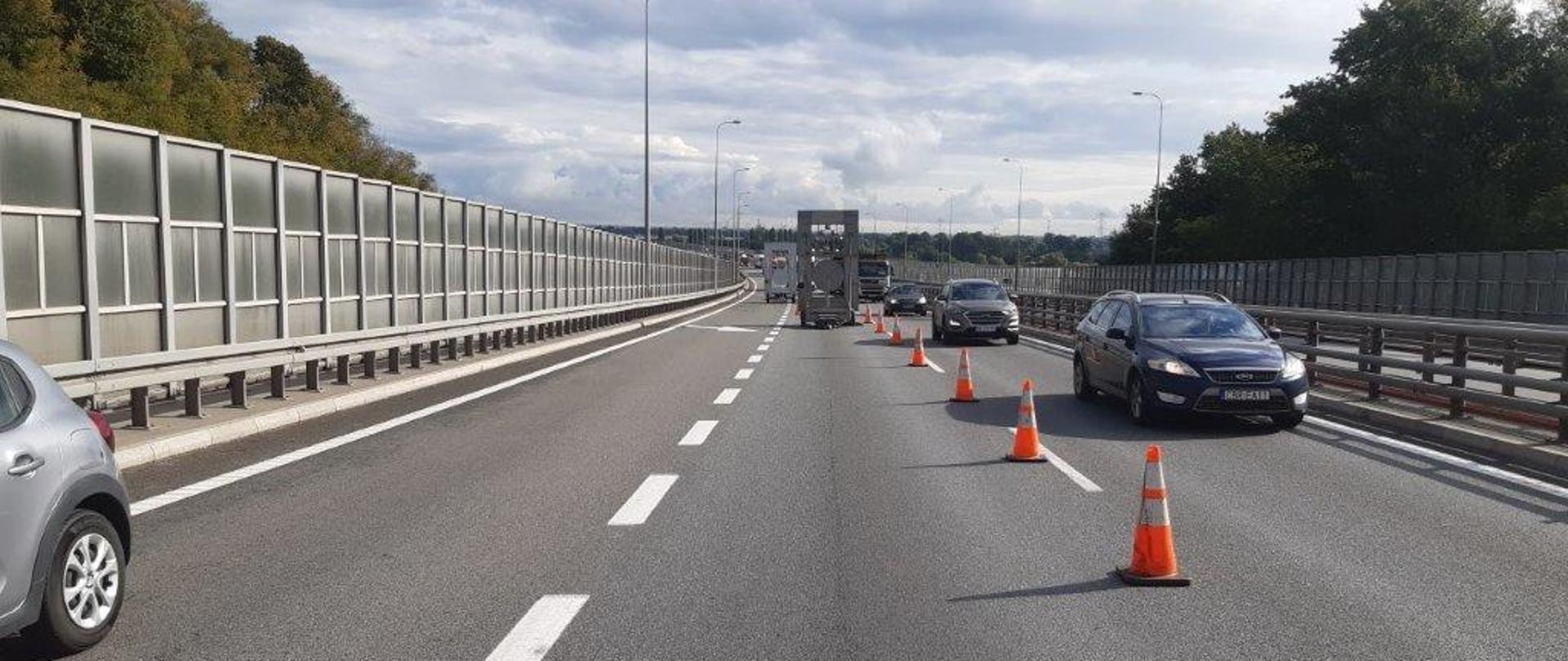 Widok na drogę ekspresową S7 - Południowa obwodnica Gdańska. Widoczne zwężenie jezdni, ustawione pachołki i znak ostrzegający o zwężeniu. Samochody są kierowane na skrajny lewy pas w kierunku obwodnicy Trójmiasta.