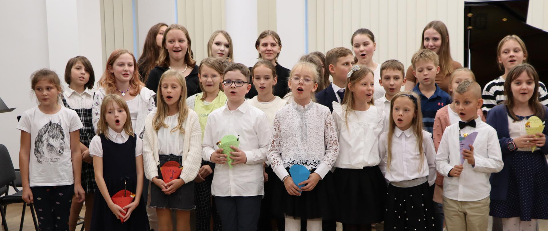 Zakończenie koncertu. Uczniowie i uczennice szkoły muzycznej stoją na środku sali