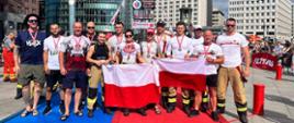 Uczestnicy Strażak podczas jednej z konkurencji na zawodach 18 Firefighter Combat Challenge Berlin pozują z flaga Polski do pamiątkowej fotografii.