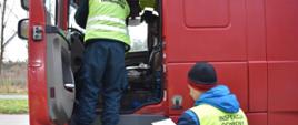 Pracownik Inspekcji Transportu Drogowego stoi na schodkach kontrolowanego samochodu ciężarowego, przy samochodzie stoi pracownik Inspekcji Ochrony Środowiska.
