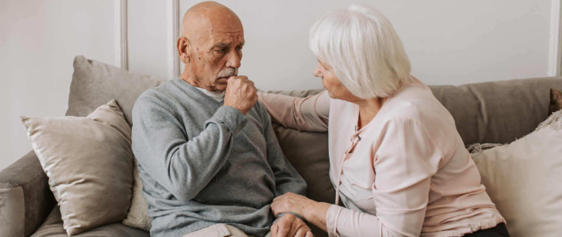 Zdjęcie przedstawia starszego mężczyznę chorującego najprawdopodobniej na astmę. Obok niego siedzi starsza kobieta, która czule się nim opiekuje.
