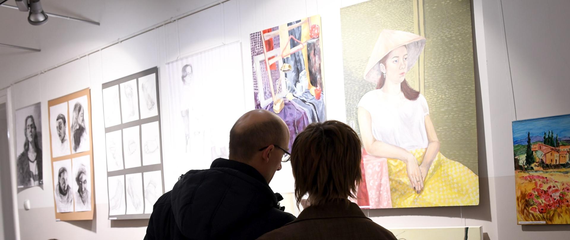 Zdjęcie przedstawiające ludzi oglądających prace malarskie na wystawie